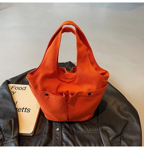 Detailed view of an orange canvas tote bag featuring pleated front pockets and black buttons