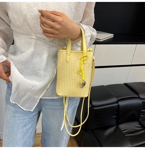 Dettaglio della trama in pelle intrecciata giallo chiaro e ciondolo a cuore sulla borsa