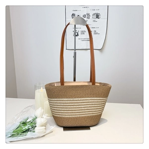 Detail of woven straw bucket tote bag with khaki stripes and brown leather strap