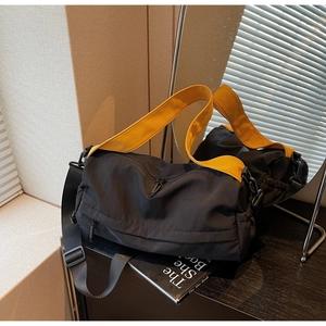 Detail of spacious black nylon crossbody bag featuring a vibrant yellow woven strap
