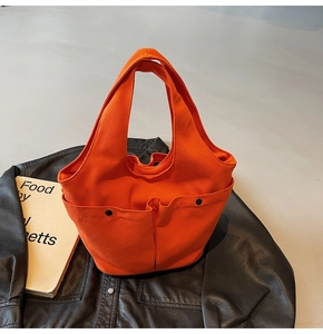 Detail of bright orange canvas tote bag showing double exterior pockets with black snaps