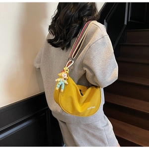 Detail of yellow crescent crossbody bag with colorful woven strap and cartoon pendant