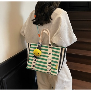 Detail view of large canvas tote bag with green stripes and yellow smiley face charm