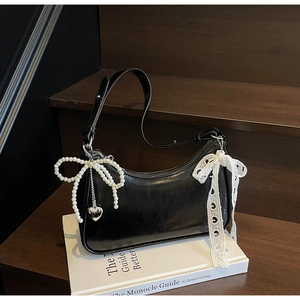 Dettaglio borsa a mezzaluna nera lucida con fiocco di perle e ciondolo a cuore