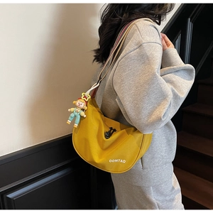 Detail of yellow nylon hobo bag with striped shoulder strap and cute cartoon doll pendant