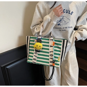 Detail of green and white striped canvas tote bag with lettered handle and smiley pendant