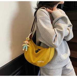 Detail of yellow crescent crossbody bag featuring wide striped strap and doll charm