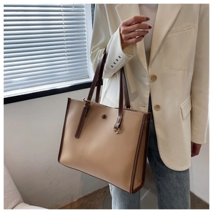 Detail of a large beige tote bag with brown straps styled with a white blazer
