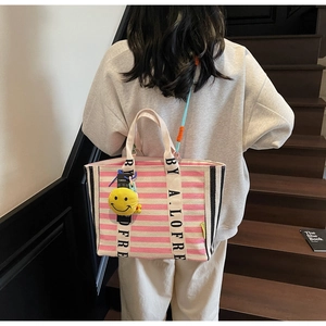 Macro view of striped canvas tote with logo webbing strap and smiley face charm