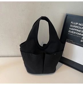 Detail of black canvas tote bag showing three front pockets and metal button closures