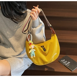 Detail of yellow crescent canvas bag featuring striped wide strap and charm on wood background