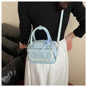 Detail of light blue crossbody pillow bag with white lace and checkered bow on a model