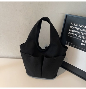 Close-up of black canvas tote bag showing large side pockets and metal button details