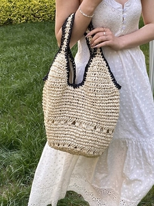 Handwoven straw shoulder bag with black trim and hollow pattern on green lawn
