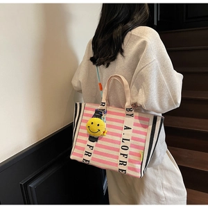 Detail view of large striped canvas tote bag with pink stripes and yellow smile charm