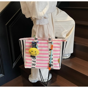 Macro detail of pink striped canvas tote bag featuring lettered webbing straps and smiley charm
