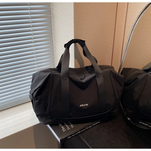 Détail du sac de sport noir avec logo NOCO et double fermeture sur une table en bois