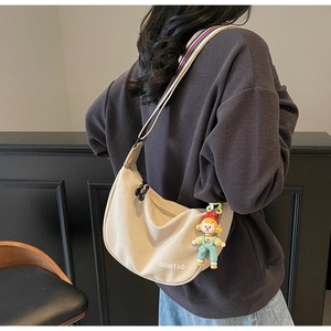 Detail of beige crescent crossbody bag with colorful striped strap and cute doll pendant