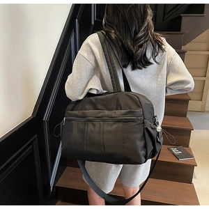 Rear view of a model carrying a black nylon travel tote bag on a modern staircase