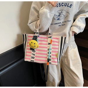 Detail of pink striped canvas tote bag featuring lettered handles and a smiley face charm