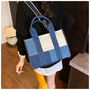 Detail of color-block denim tote bag with wide shoulder strap in a cozy indoor setting