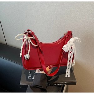 Dettaglio borsa hobo in vernice rossa con fiocco in pizzo bianco e ciondolo a cuore