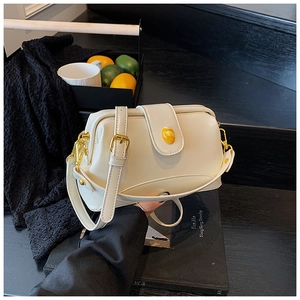 Gros plan du sac à bandoulière en cuir verni blanc avec fermoir ambre sur des marches sombres