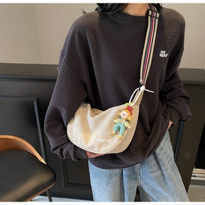 Detail of beige crossbody dumpling bag with colorful striped strap and cute doll pendant