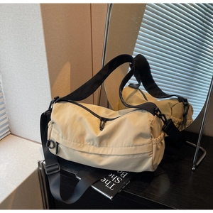 Detail view of beige nylon cylinder bag with black adjustable strap and front zip pocket