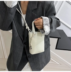 Dettaglio della mini borsa a tracolla bianca intrecciata con ciondolo a cuore e pelle