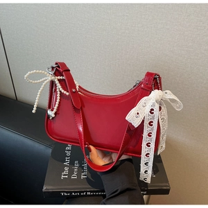 Dettaglio della borsa in pelle verniciata rossa con ciondolo a cuore e fiocco in pizzo