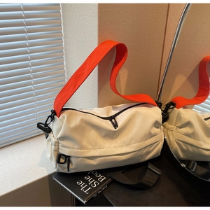 Detail of off-white crossbody bag with bright orange strap and dual zipper closure