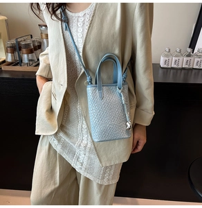 Dettaglio della borsa azzurra con trama a coccodrillo e ciondolo argento su modella