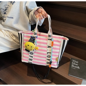 Detail of striped canvas tote bag with pink stripes and cute plush yellow smiley charm