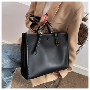 Detail of black tote bag with white contrast stitching and golden metal hardware accents