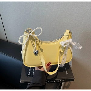 Dettaglio borsa hobo gialla con fiocco di perle, ciondolo a cuore in metallo e pizzo