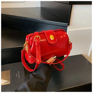 Détail du sac bandoulière rouge brillant avec garniture dorée et boucle jaune ovale
