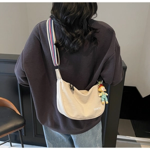 Detail of off-white dumpling bag with striped wide shoulder strap and cartoon charm