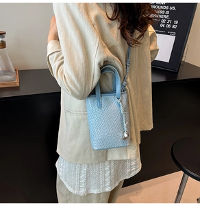 Modella che indossa una borsa tote azzurra a trama intrecciata con tracolla e ciondolo