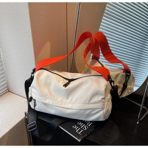 Detail view of the white sporty pillow bag with orange webbing and multiple functional pockets