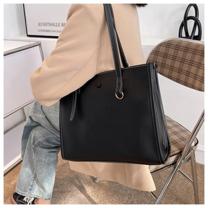 Detail view of black tote bag with white contrast stitching and metallic ring accent