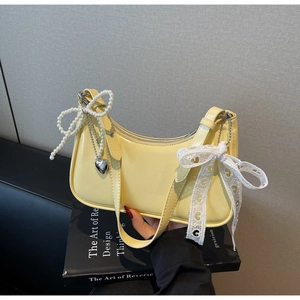 Dettaglio borsa hobo gialla con fiocco di perle, nastro di pizzo e ciondoli a cuore