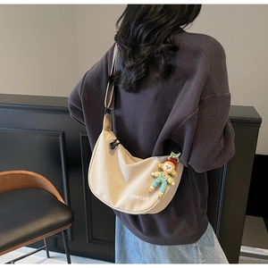 Detail view of beige crescent bag with colorful striped strap and cartoon charm decoration