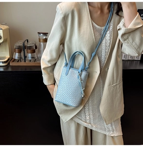 Dettaglio mini tote bag azzurra a trama intrecciata con ciondolo a pompon e tracolla