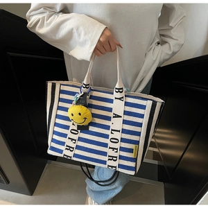 Detail of blue and white striped canvas tote bag with lettered handle and yellow charm