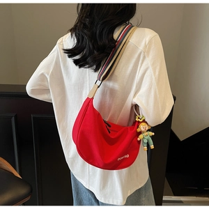 Detail of red crescent canvas bag featuring colorful woven strap and decorative doll charm