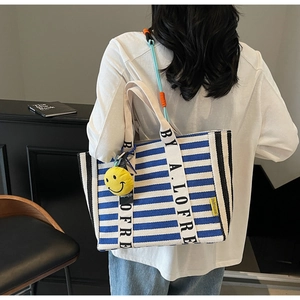 Detail view of large striped canvas tote bag with logo handle and yellow smiley face charm