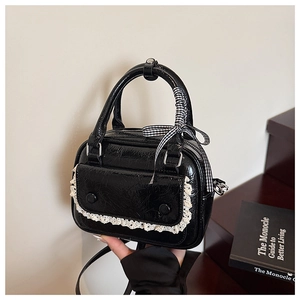 Detail of glossy black handbag with white lace trim and checkered ribbon decoration