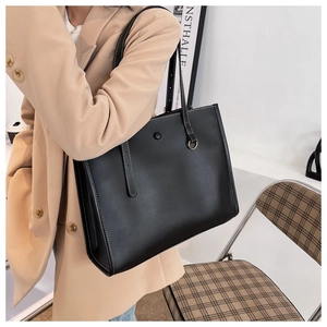 Detail of a black leather tote bag featuring contrast stitching and a round metal buckle