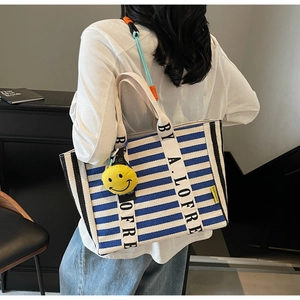 Detail of blue striped canvas tote bag with black piping and yellow smiley charm